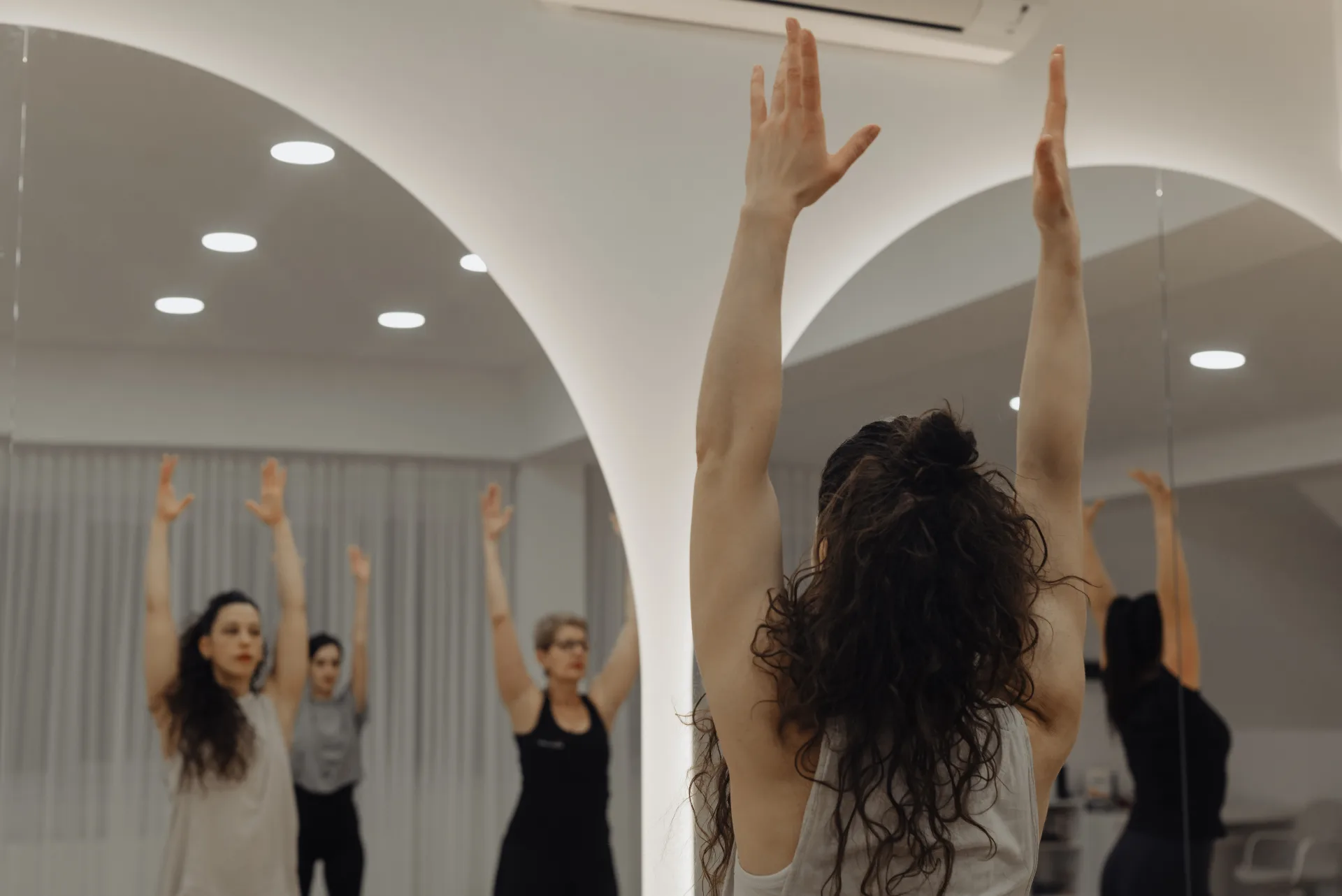 Clasă de grup la The Studio — brațe ridicate în studio cu oglinzi arcuite